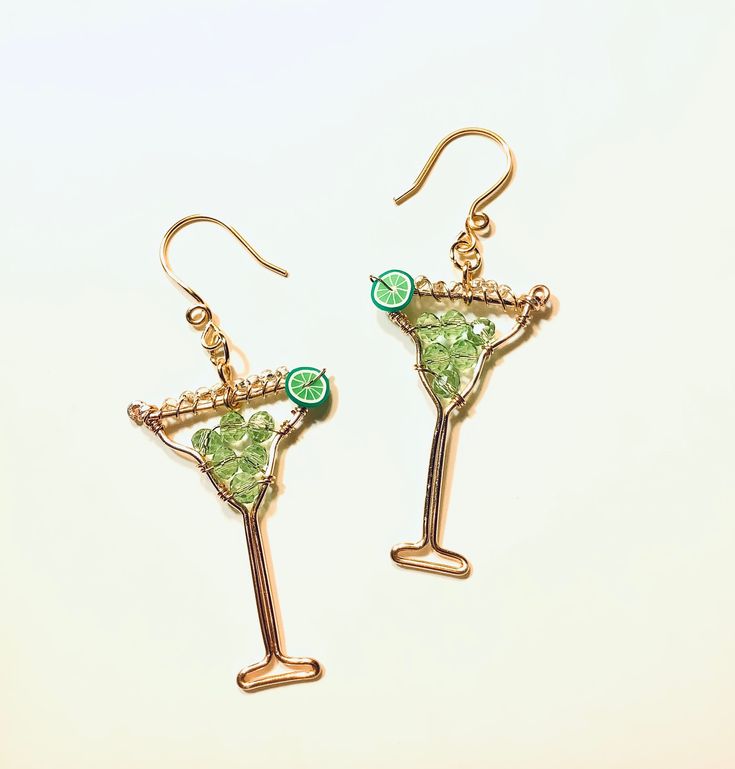 a pair of earrings featuring a martini glass with green garnish on the side