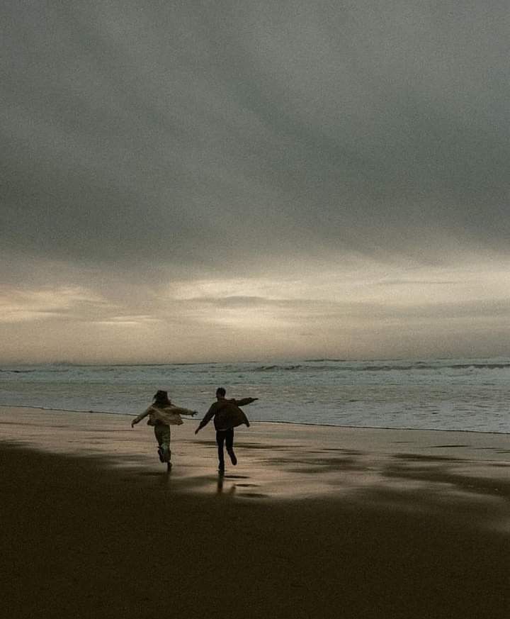 two people running on the beach with their surfboards