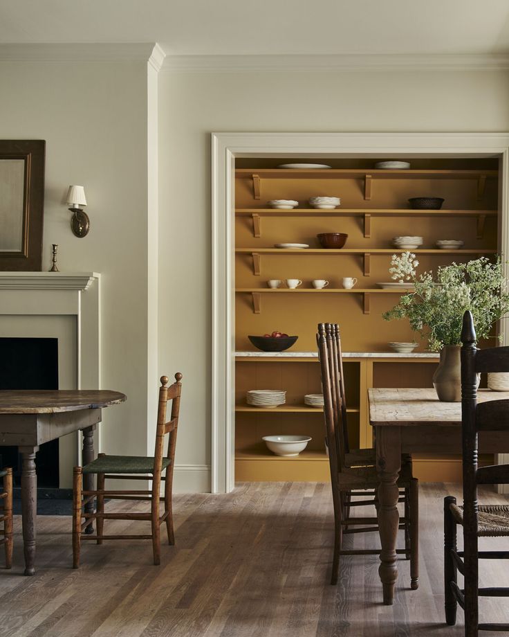 a dining room table and chairs in front of a fireplace with shelves on the wall