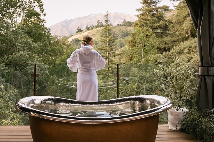 a woman in a bathrobe standing next to a large copper tub on a deck