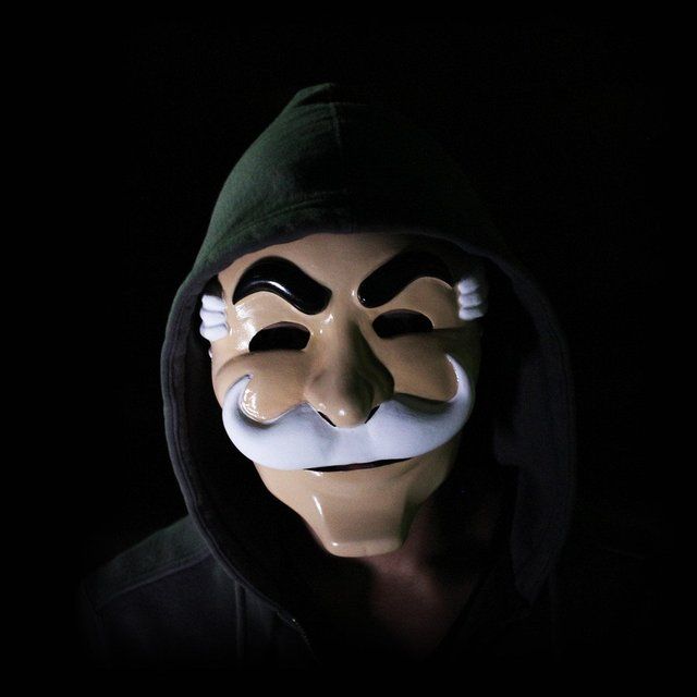 a person wearing a mask and hood in the dark with a moustache on their face