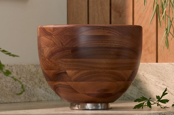 a wooden bowl sitting on top of a counter next to a potted green plant