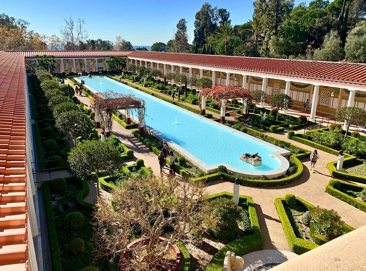 an aerial view of a pool surrounded by greenery and red tiled roofing area