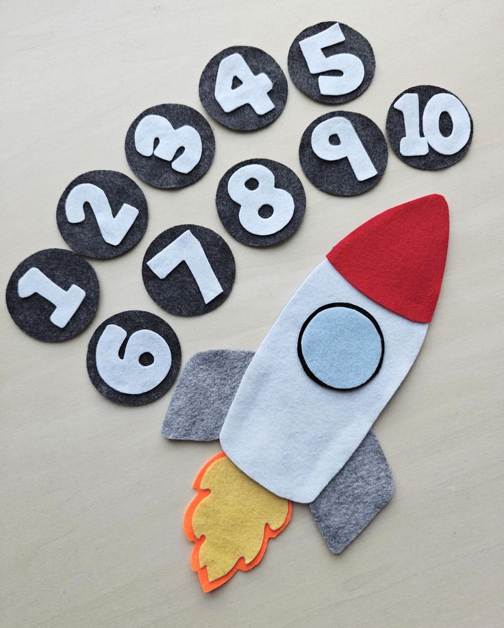 a felt rocket with numbers on it sitting next to magnets that spell out the time