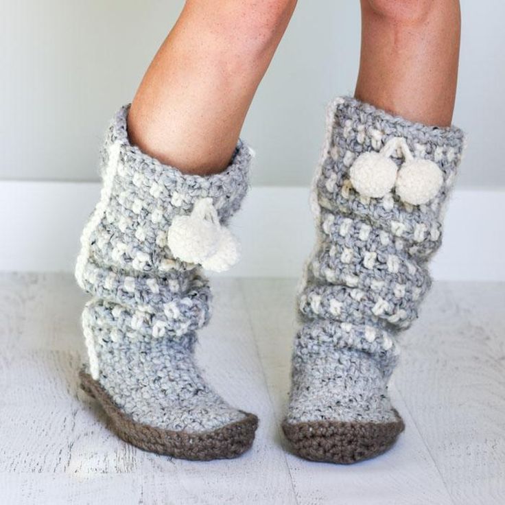 the legs and feet of a woman wearing knitted slippers with pom poms