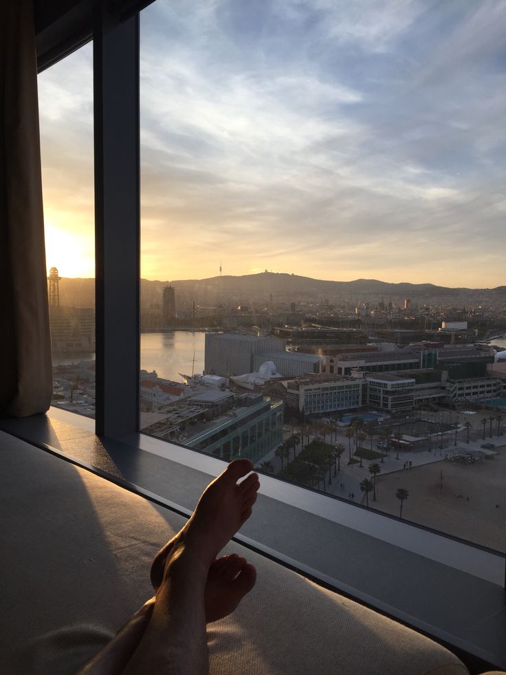 a person's hand on the edge of a window looking out at a city