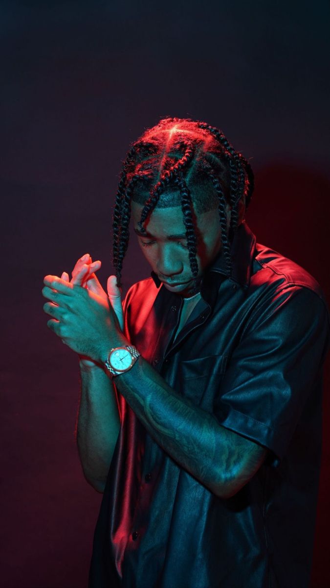 a man with dreadlocks standing in front of a dark background holding his hands together