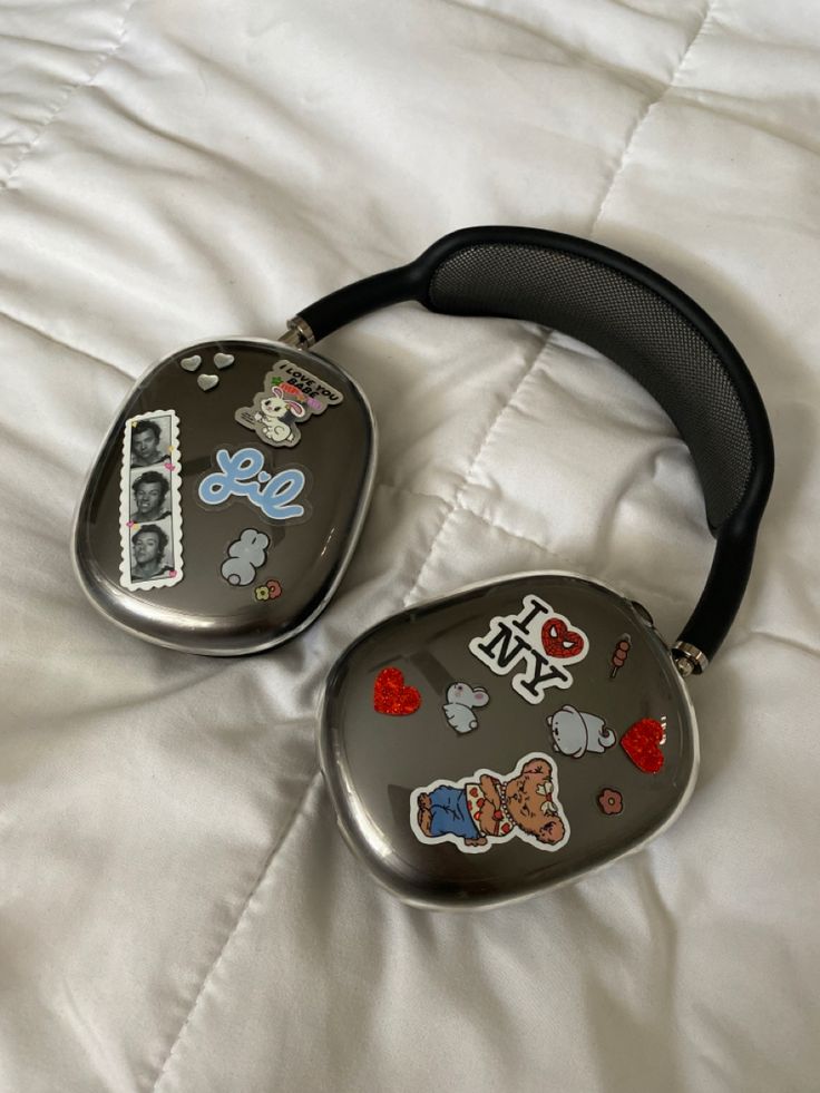 two black and silver items laying on top of a white bed covered in sheets with mickey mouse stickers