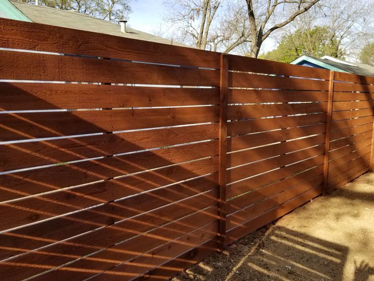 a wooden fence that is next to a house with trees in the background and shadows on the ground