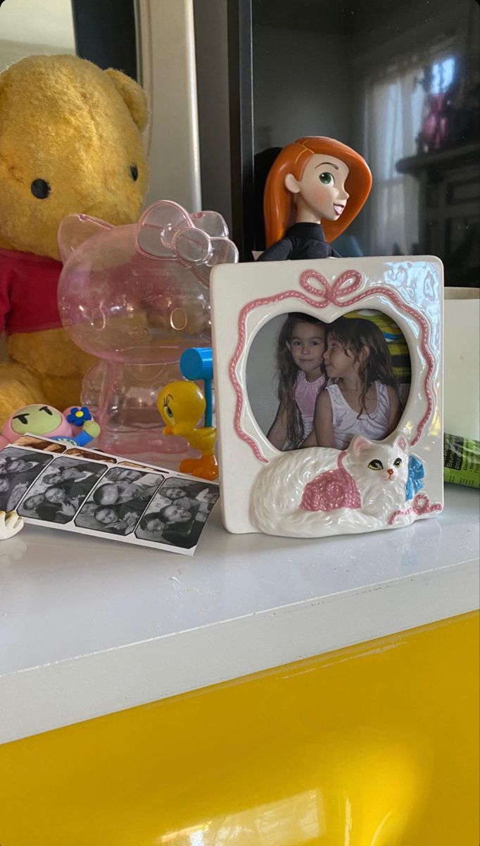 a teddy bear sitting on top of a counter next to a photo frame and other toys