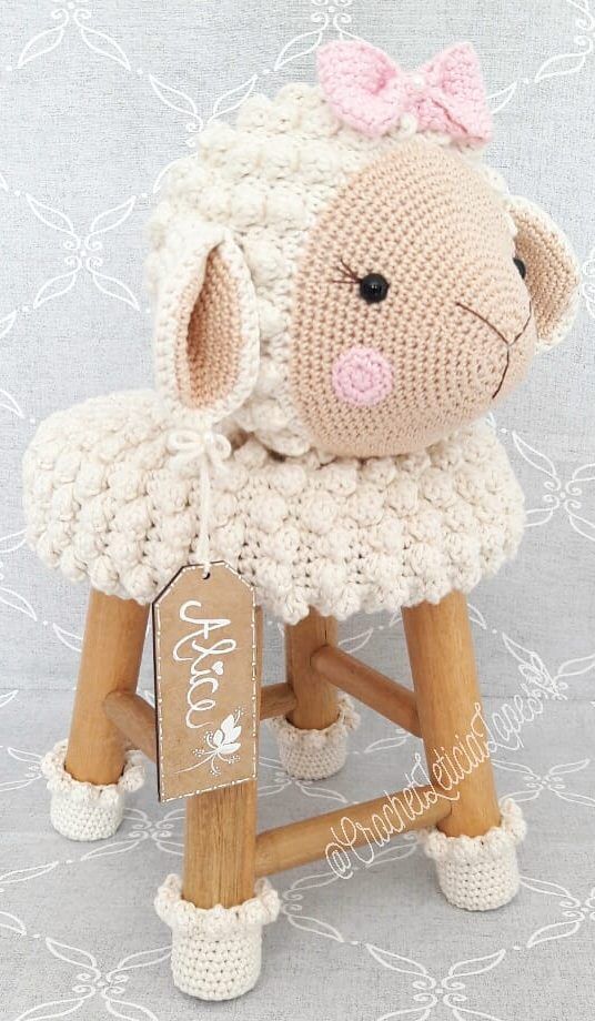 a crocheted sheep sitting on top of a wooden stool with a name tag