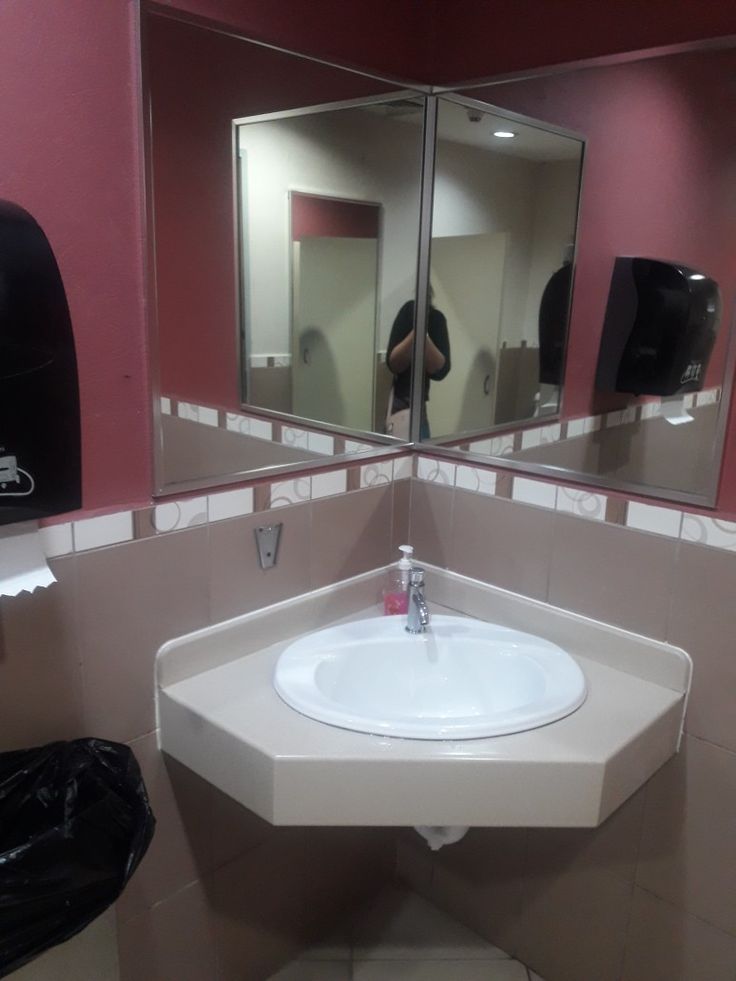 a white sink sitting under a bathroom mirror next to a trash can and paper towel dispenser