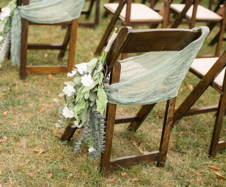 the chairs are set up with green sashes and flowers on them for an outdoor ceremony