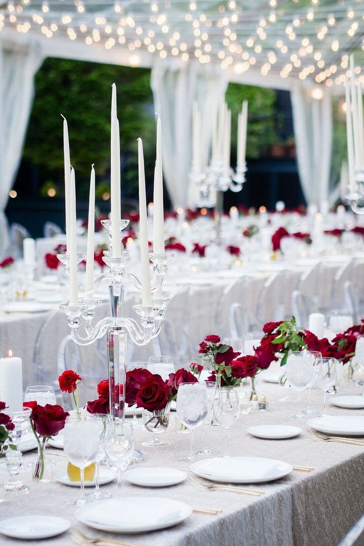 the tables are set with white and red flowers, candles, and place settings for dinner