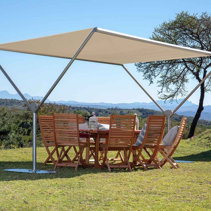 a table and chairs under an awning on top of a grass covered field with mountains in the background