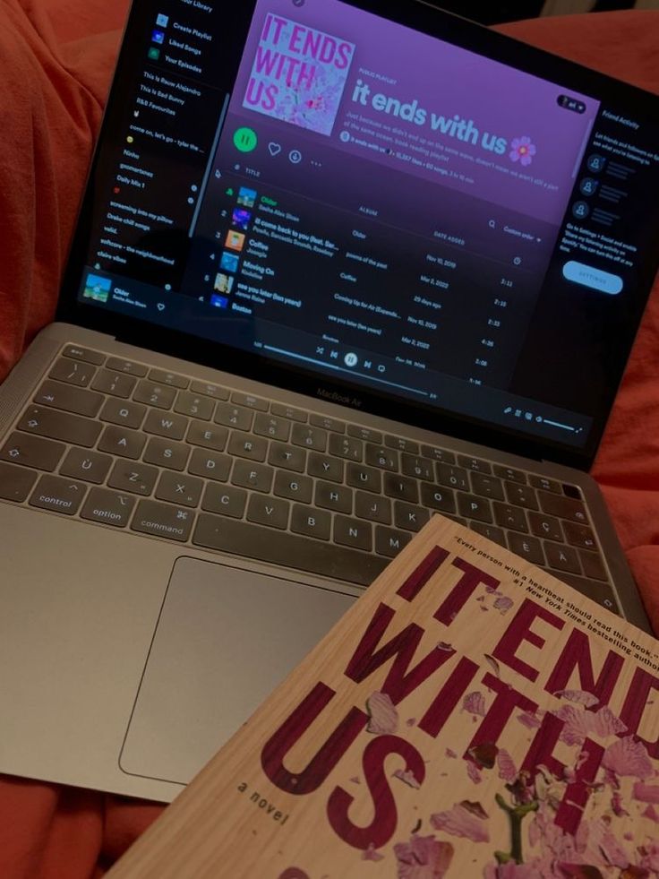 an open laptop computer sitting on top of a bed next to a book titled it ends with us