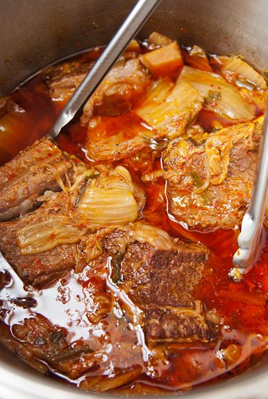 a pot filled with meat and vegetables being stirred by two tongs in the pot