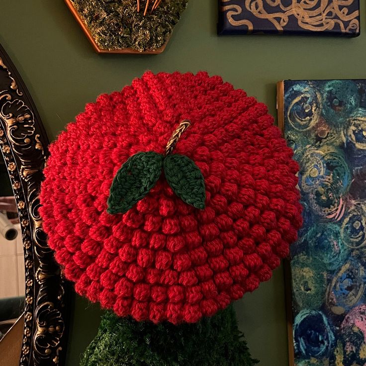 a crocheted pomegranate hanging on the wall in front of paintings