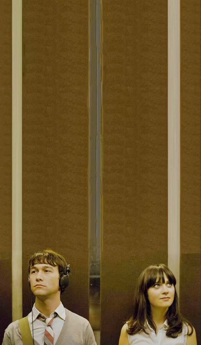 two people standing next to each other in front of a tall wall with vertical blinds