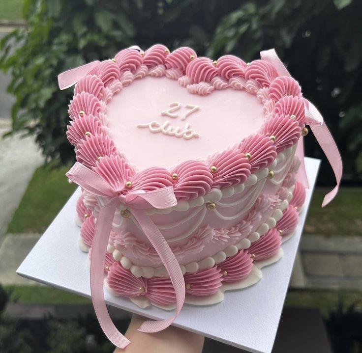 a heart shaped cake with pink icing and bows on it's edges is being held by a person