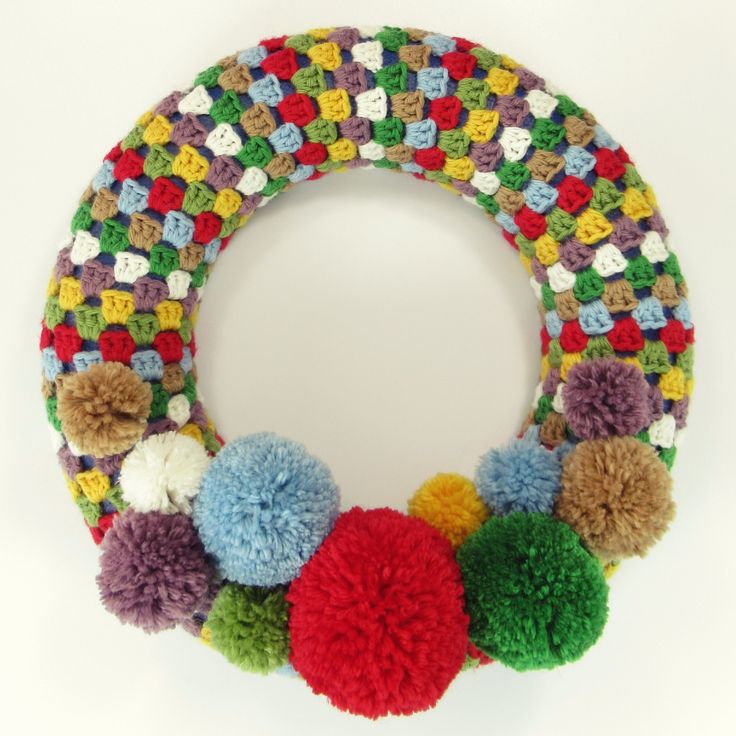 a multicolored knitted wreath with pom - poms hanging from it