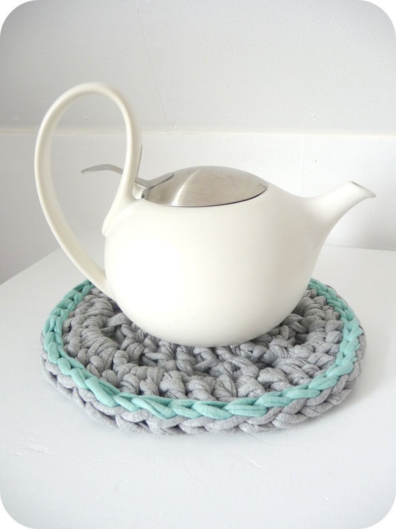 a white tea pot sitting on top of a crocheted coaster