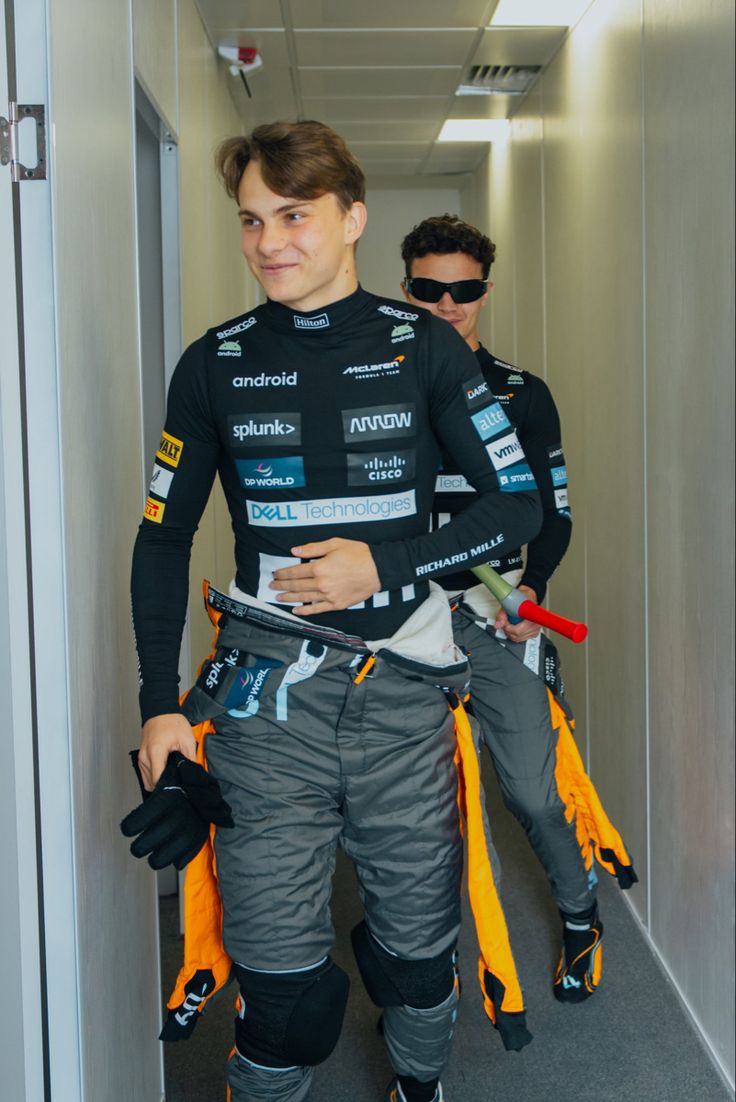 two men walking down a hallway with safety equipment on their back and one man in the background