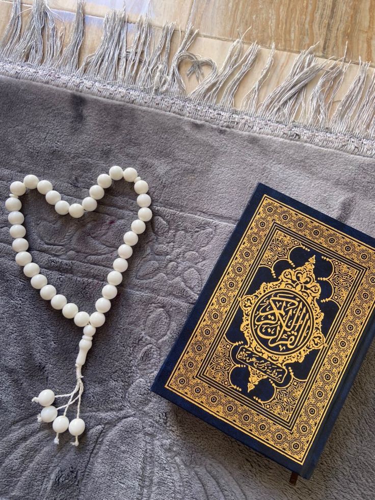 a rosary, book and tassel on a gray blanket with a heart shaped bead necklace