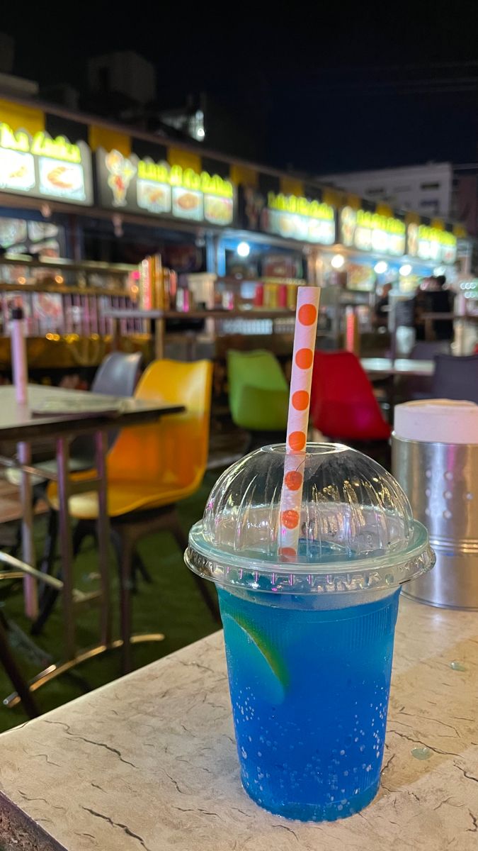 a blue drink sitting on top of a table next to a cup with a straw in it