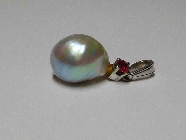 This is 18kt white gold white with strong bluish grey rose overtones in color Cultured ? Pearl and Natural Ruby Corundum gemstone pendant with medium size bail. The very fine quality transparent in Clarity, Red Color Excellent Faceted Round Cut Ruby gemstone measures and weighs approximate 3.0 mm weighing .10 points carat total weight. The Cultured ? Pearl has white with strong gray bluish rose overtone's in color, measure 1/3 inch x 1/2 inch in Size, natural oblong shape, excellent luster, moderate naturally blemished surface quality and acceptable nacre. It appears to have some type of glue at top of pearl attached to pendant. This very old pendant has a bail stamped 750 and in very good condition. Condition of this fine quality Ruby and Cultured Pearl pendant is excellent and weight 2.2 White Gold Drop Jewelry With High Luster, Platinum Drop Jewelry Gift, White Gold Drop Earrings With High Luster, Elegant Silver Pear-shaped Gemstones, Pear-shaped Platinum Jewelry As Gift, High Luster White Gold Drop Jewelry, Silver Drop Jewelry With High Luster, White Gold Gemstone Pendant For Formal Occasions, High Luster Silver Drop Jewelry