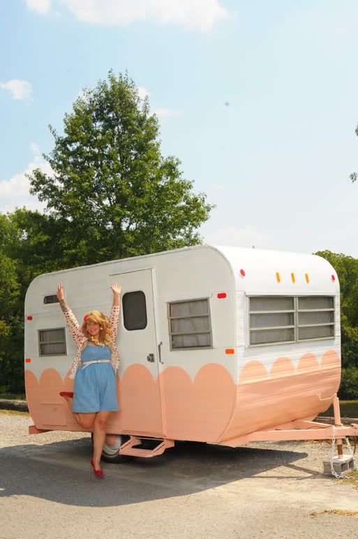 a woman standing in front of a pink and white trailer