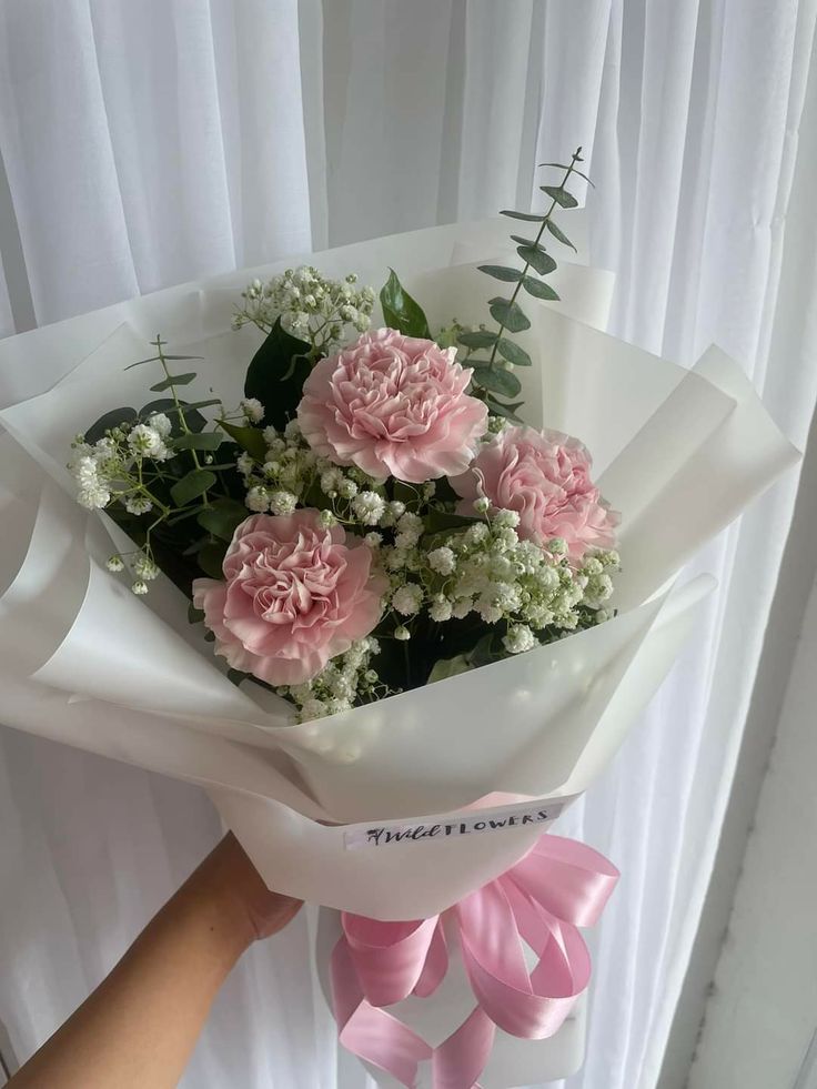 a bouquet of pink carnations and baby's breath in front of a white curtain