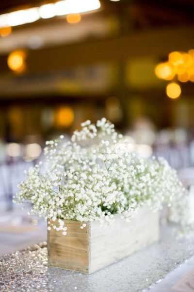 small white flowers are in a wooden box on the table at a wedding or reception