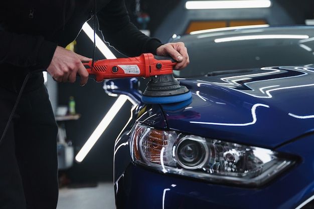 a car being worked on by a man with an electric polisher in his hand