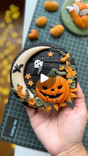 a hand holding a cookie decorated like a halloween moon and jack - o'- lantern