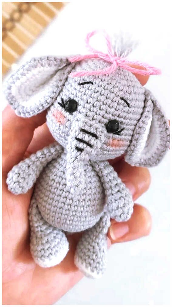 a small crocheted elephant with a pink bow on its head sitting in someone's hand