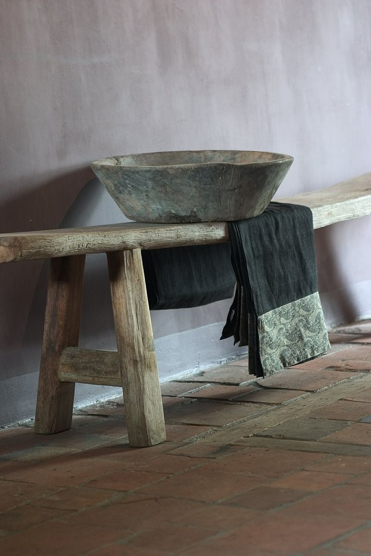 a stone bowl sitting on top of a wooden bench next to a brick floor and wall