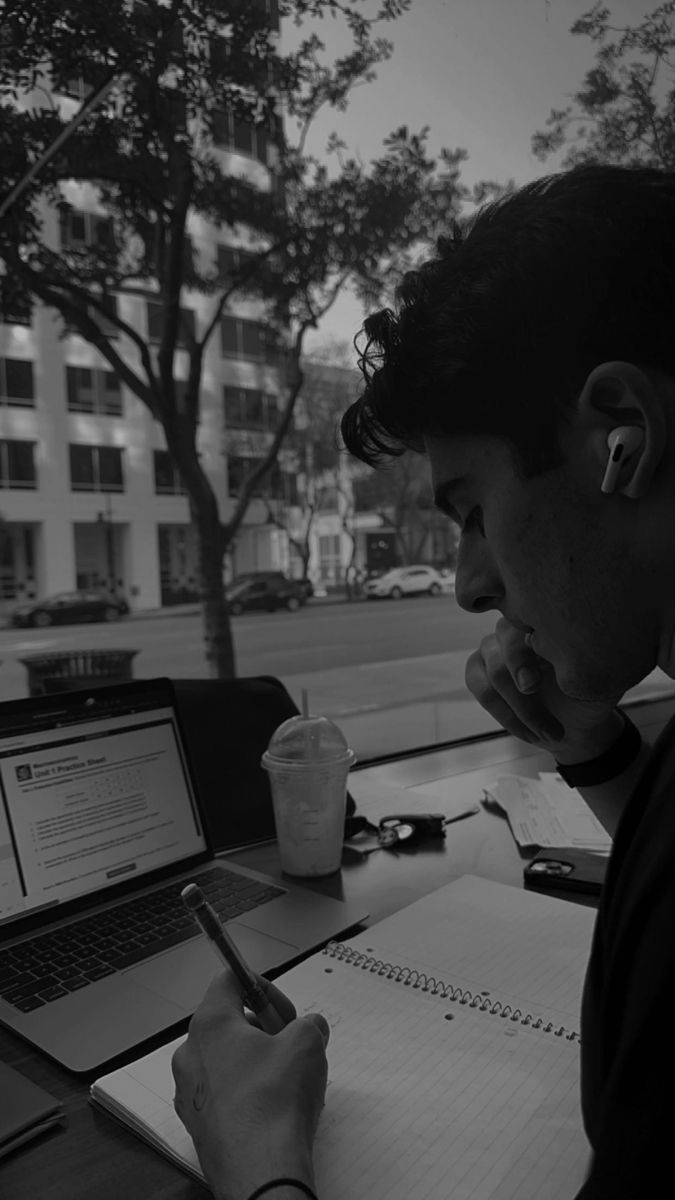 a man sitting at a table with a laptop and pen in his hand, writing on paper