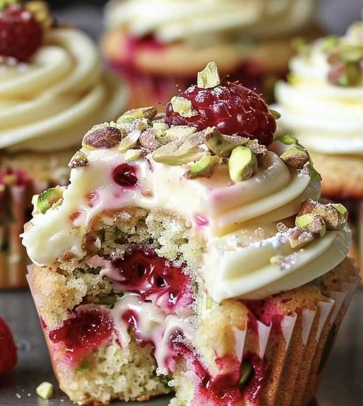 cupcakes with white frosting, raspberries and pistachio on top