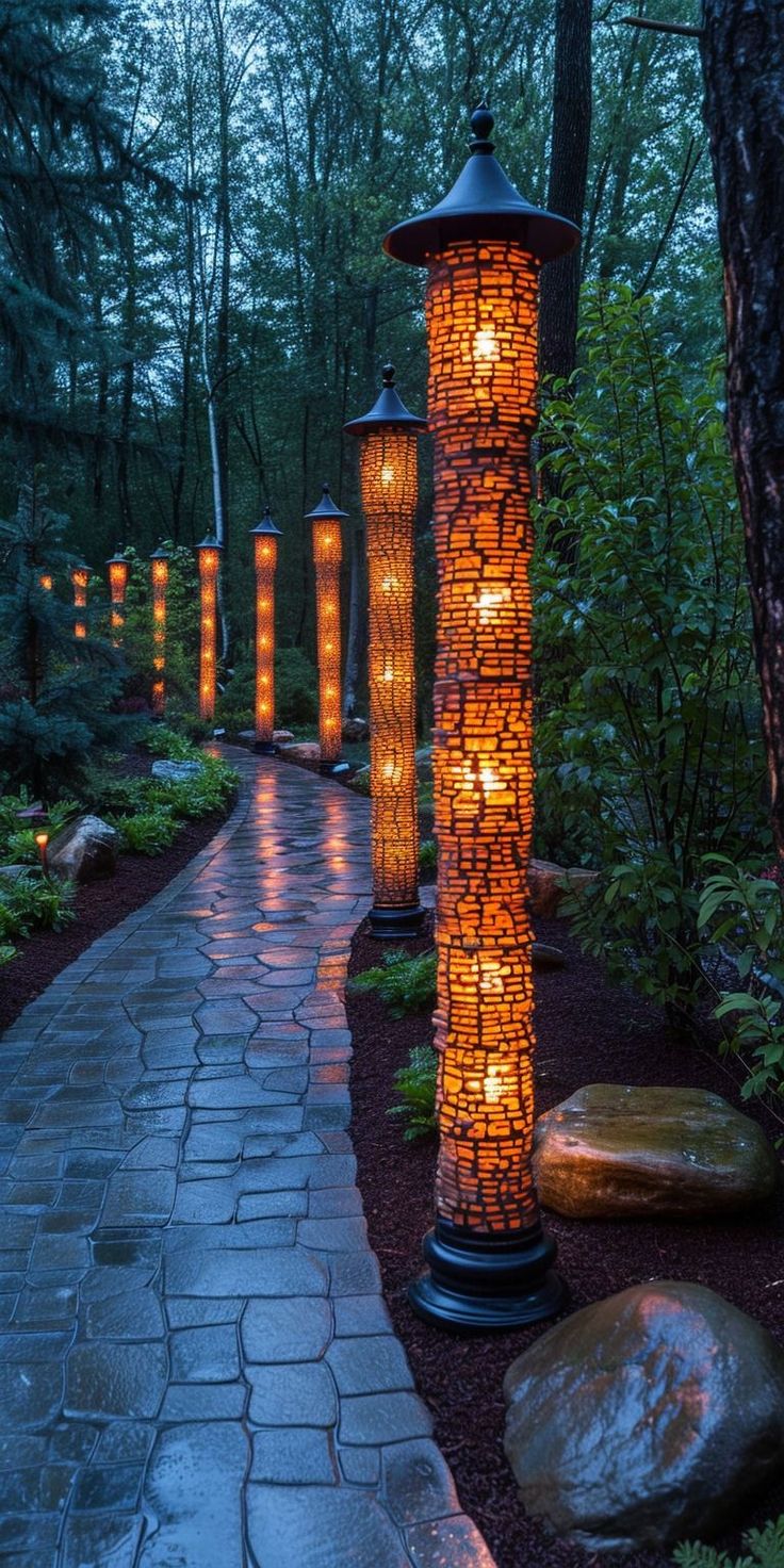 an outdoor path with lanterns lit up at night in the woods, surrounded by rocks and trees