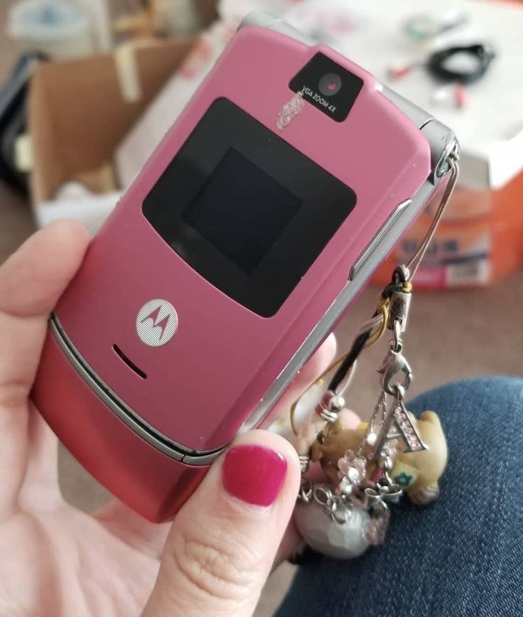 a person holding a pink cell phone in their hand with a key chain attached to it