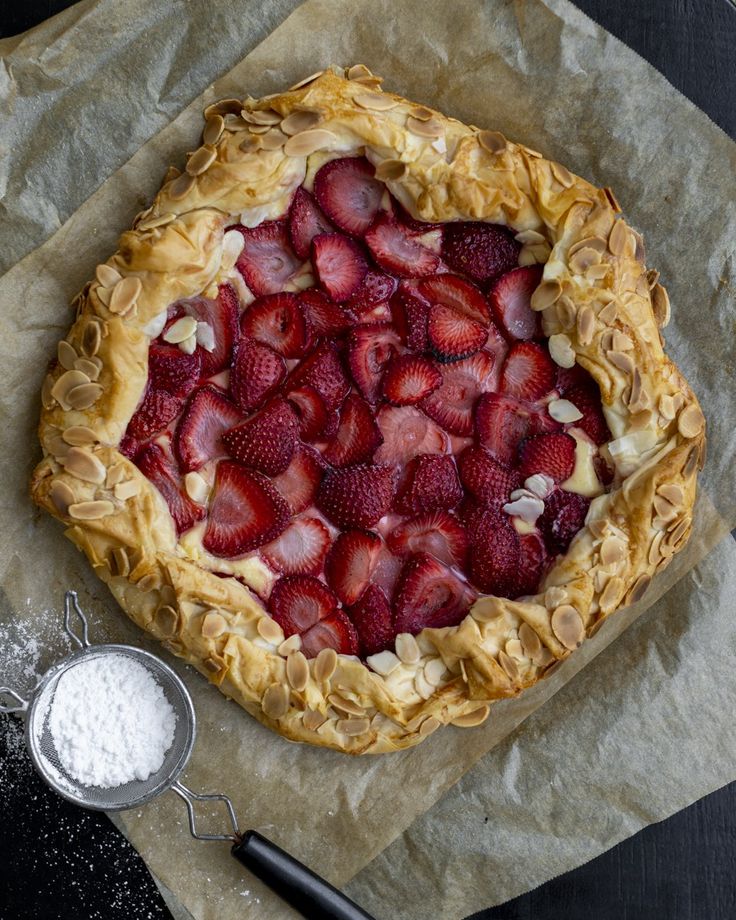 a pie topped with strawberries on top of parchment paper