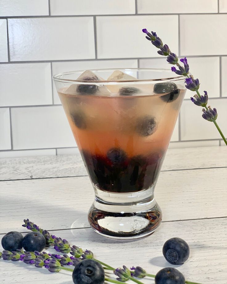 a glass filled with ice and blueberries on top of a table next to flowers