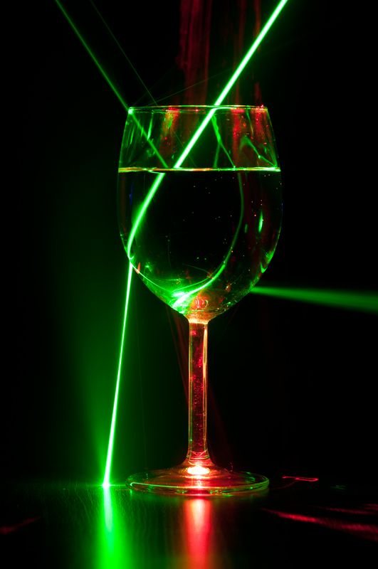 a wine glass sitting on top of a table next to a green laser light in the dark