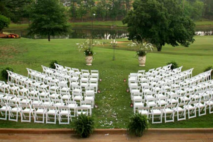 rows of white chairs set up for an outdoor wedding ceremony in front of a golf course