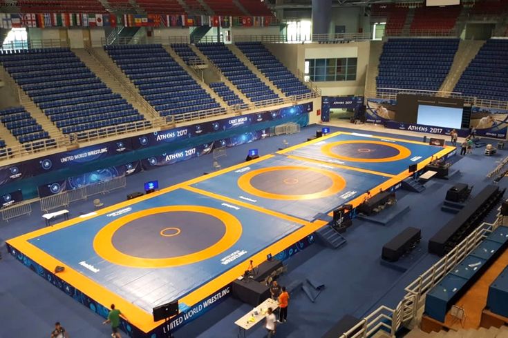 an indoor wrestling court with blue and yellow mats on the floor, surrounded by rows of empty bleachers