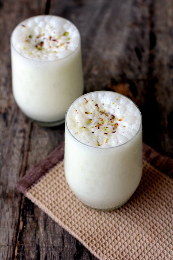 two glasses filled with white liquid sitting on top of a wooden table next to each other