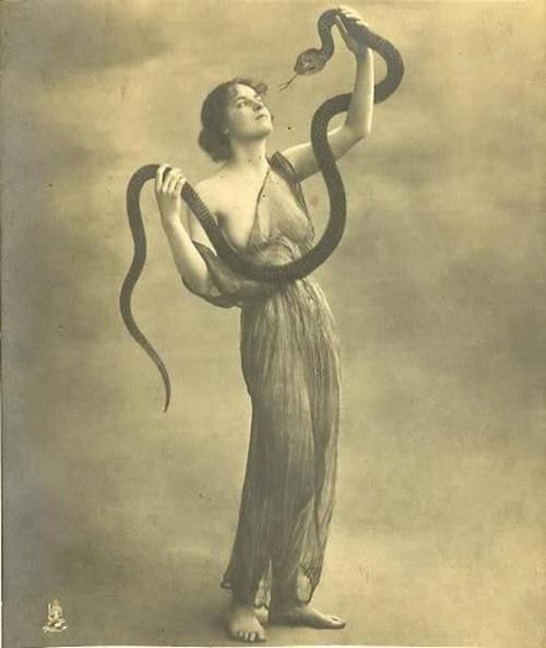 a woman holding a snake in her right hand and looking up at it's tail