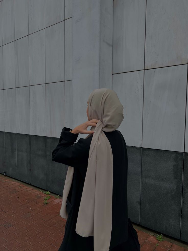 a woman wearing a hijab walking down the street in front of a building