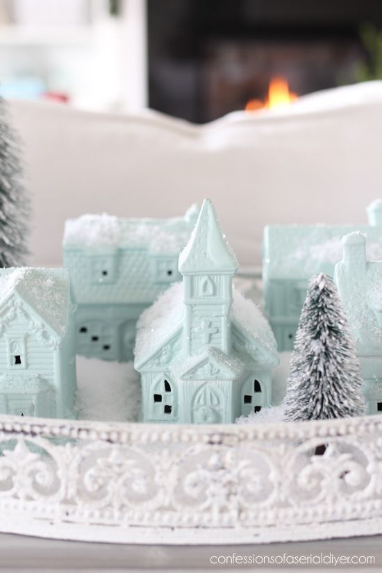 a white tray with some small houses and trees in it on a table next to a couch